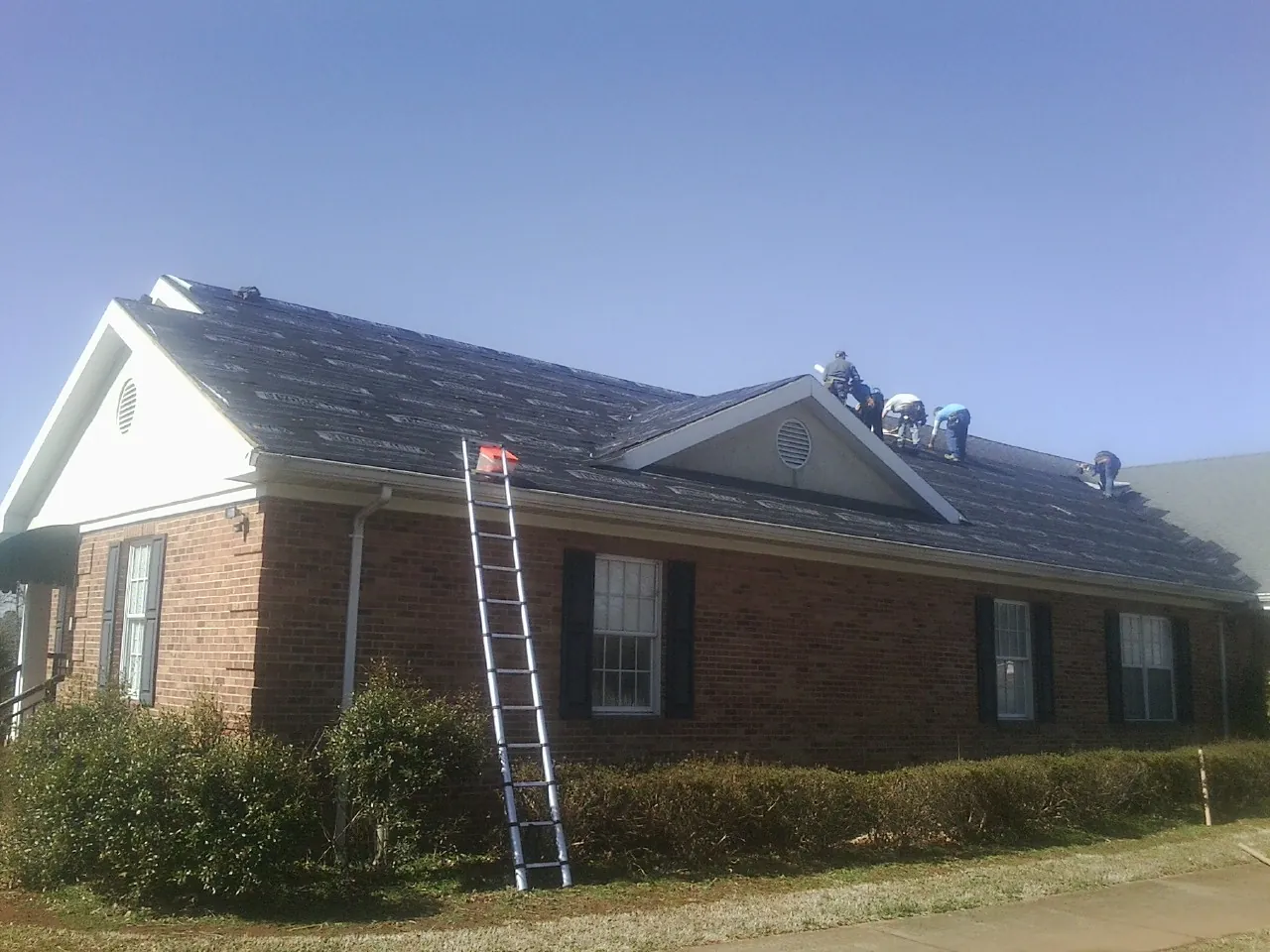 Crew tearing shingles off a brick ranch roof with a ladder set — Metal Roof Repair work by our crew in Garibaldi