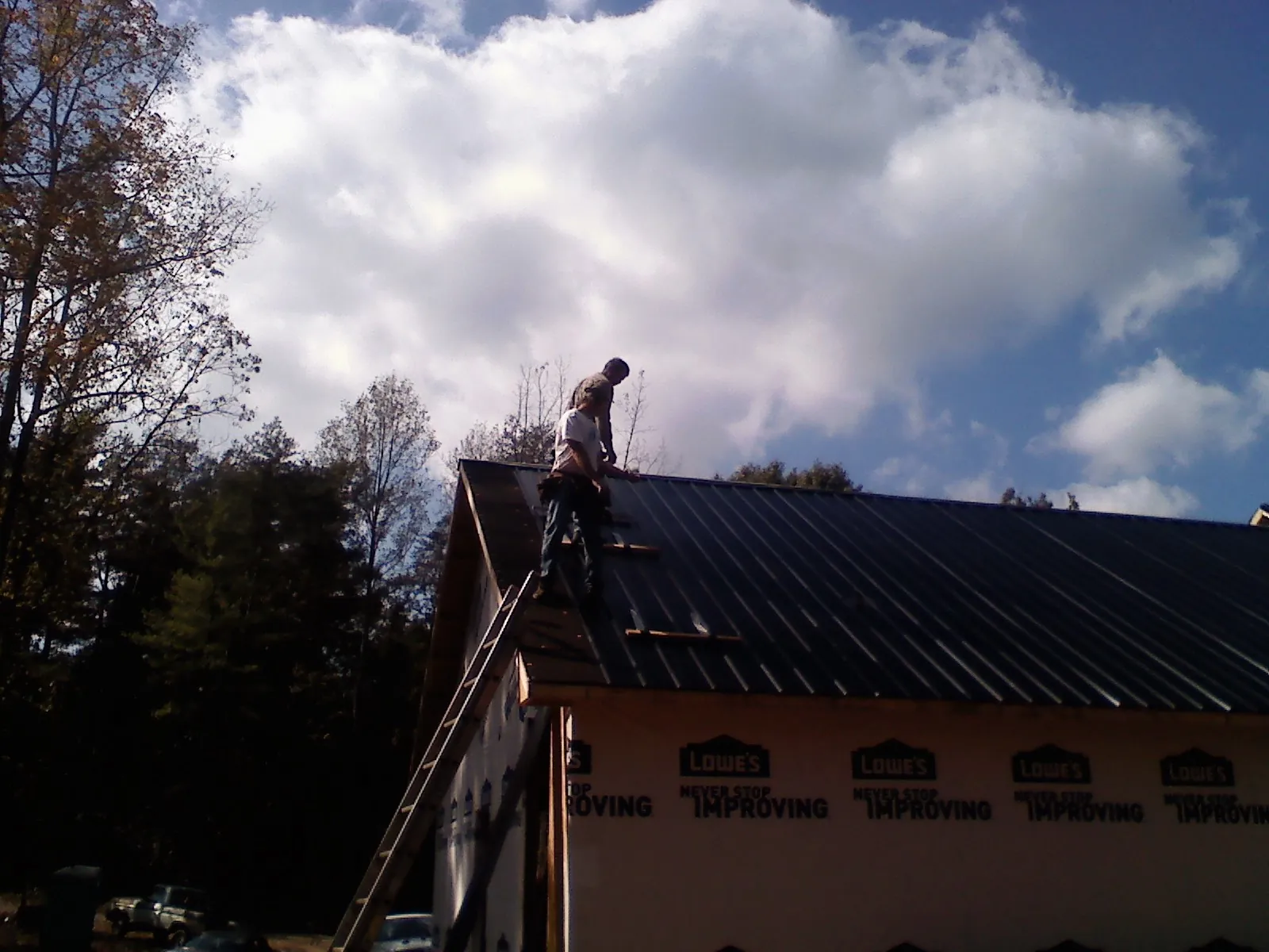 Roofer fastening dark metal panels high against a cloudy sky, from a Roof Inspection job in Garibaldi